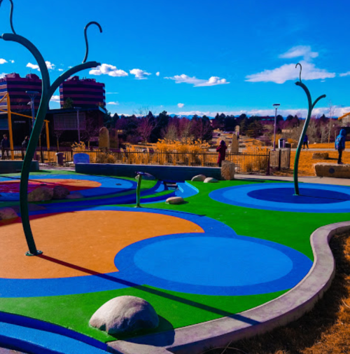 Colorful playground with blue and orange areas, green accents, and rocks, set against a clear blue sky.