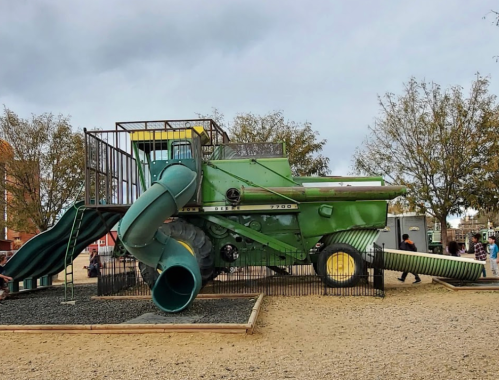 A playground featuring a large green combine harvester structure with slides and climbing areas for children.