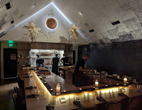 A modern restaurant interior with a central bar, chefs at work, and ambient lighting creating a cozy atmosphere.