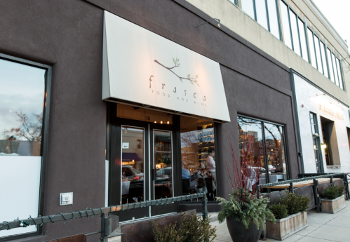 Exterior of Frasca Food and Wine restaurant, featuring a modern sign and large windows, with planters in front.