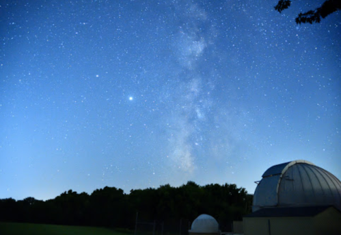 A clear night sky filled with stars and the Milky Way, with an observatory dome in the foreground.