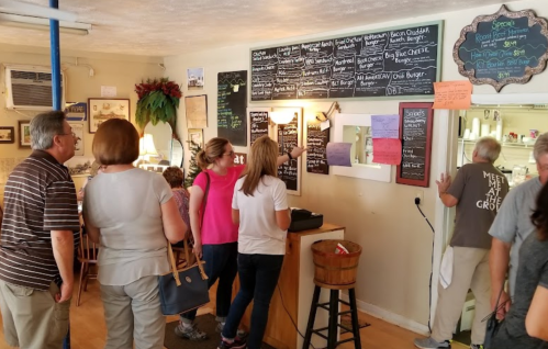 A group of people in a cozy café, looking at a menu board while one person orders at the counter.