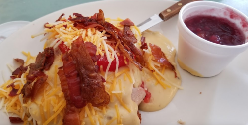 A plate of nachos topped with cheese, bacon, and tomatoes, served with a side of sauce in a small cup.