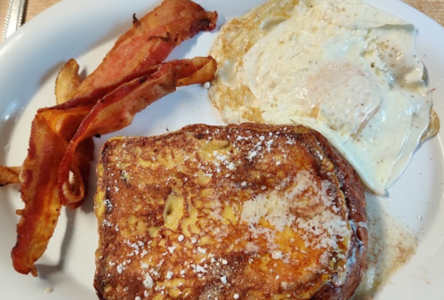 A plate with French toast, a fried egg, and crispy bacon strips.