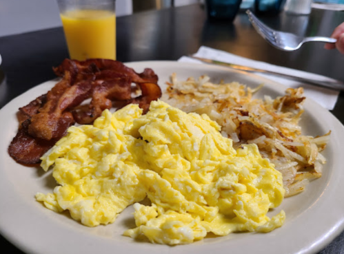 A plate with scrambled eggs, crispy bacon, and hash browns, with a glass of orange juice in the background.