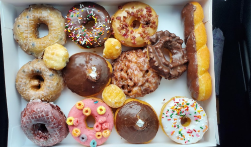 A variety of colorful donuts in a box, including glazed, chocolate, and sprinkled options, alongside a few mini donuts.