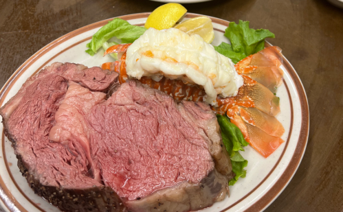 A plate featuring slices of juicy roast beef, lobster tail, and lemon on a bed of lettuce.