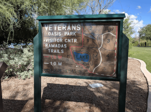 Map sign for Veterans Oasis Park, showing trails, visitor center, and lake, with distance markers.