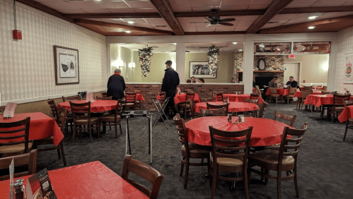 A cozy restaurant interior with red tablecloths, wooden chairs, and patrons dining in a warm, inviting atmosphere.