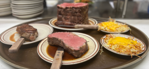 A tray with several plates of medium-rare steak, hash browns topped with cheese, and a side of sauce.