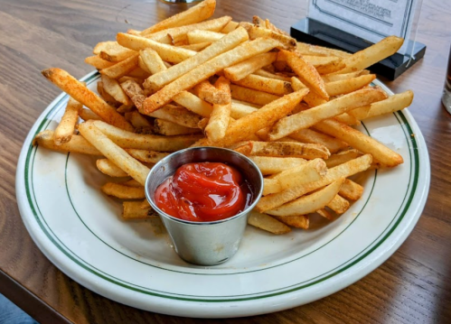 A large plate of golden French fries served with a small cup of ketchup.