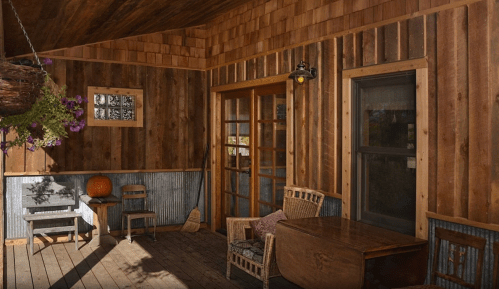 Cozy wooden porch with rustic furniture, a table, and a hanging plant, illuminated by warm light.