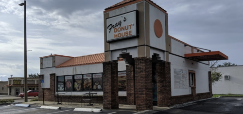 Exterior of Fran's Donut House, featuring a sign and menu boards, with a cloudy sky in the background.