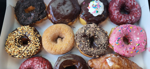 A box of assorted donuts, featuring chocolate, sprinkles, and various toppings in vibrant colors.