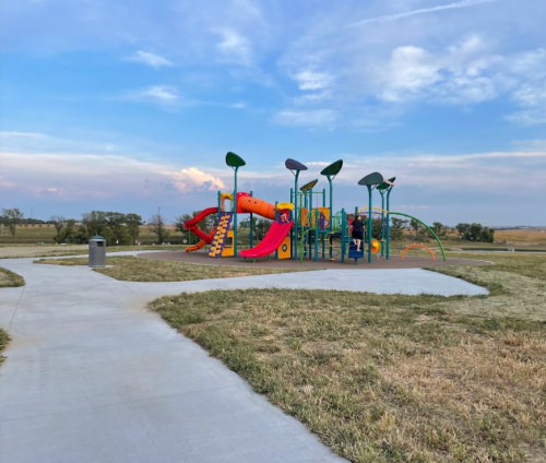 A colorful playground with slides and climbing structures, set in a grassy area under a blue sky.