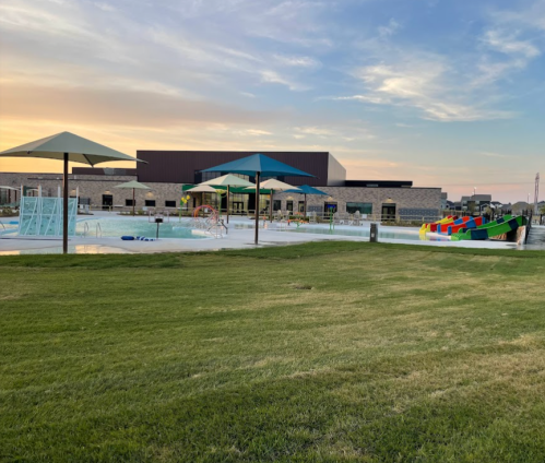 A swimming pool area with colorful umbrellas, a play structure, and a large building in the background at sunset.