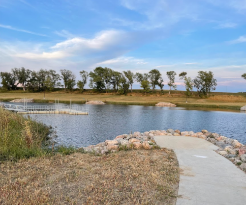 A serene landscape featuring a calm pond surrounded by trees and a stone pathway leading to the water's edge.