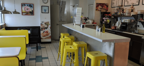 Bright diner interior with yellow stools, a counter, and floral decor. Walls feature food-themed artwork.