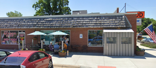 A brick building with a barber shop and outdoor seating, featuring umbrellas and an American flag nearby.