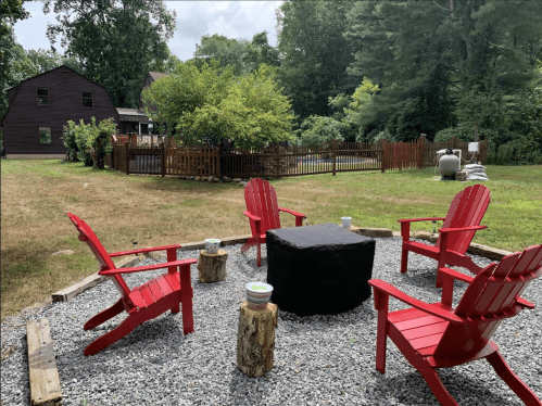A cozy outdoor seating area with four red chairs around a black table, surrounded by greenery and a wooden fence.