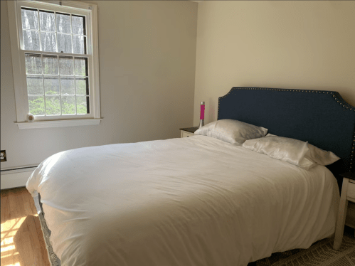 A bright, simple bedroom featuring a large bed with white bedding and a window letting in natural light.