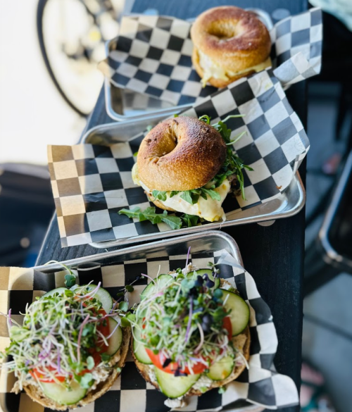 Three sandwiches on checkered paper: one bagel sandwich and two open-faced sandwiches topped with fresh vegetables.