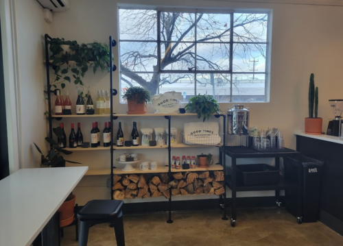 A cozy beverage station with shelves of wine, plants, and a coffee setup, next to a large window.