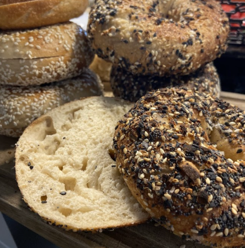 A close-up of various bagels, including sesame and everything bagels, stacked on a wooden surface.