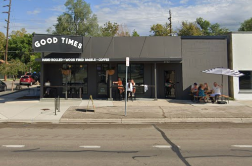 Exterior of "Good Times" café with outdoor seating, people enjoying coffee, and a striped umbrella on a sunny day.