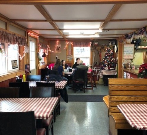 Cozy diner interior with checkered tablecloths, holiday decorations, and patrons enjoying their meals.