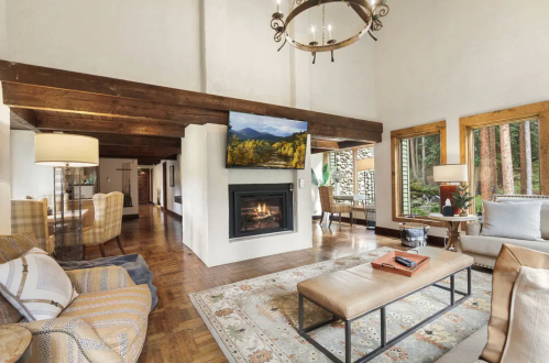 Cozy living room with a fireplace, large windows, and rustic decor, featuring a TV and comfortable seating.
