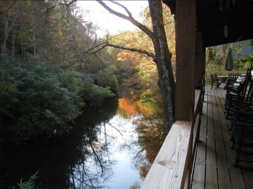 A peaceful river scene with autumn foliage, viewed from a wooden porch with rocking chairs.