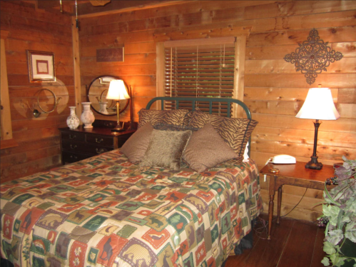 Cozy cabin bedroom with a wooden wall, a bed with patterned bedding, and warm lighting from bedside lamps.