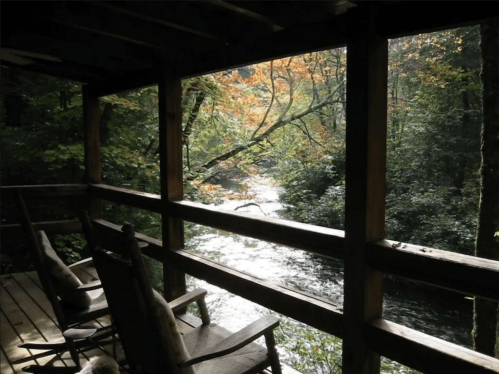 A serene view from a wooden porch overlooking a river, surrounded by trees with autumn foliage.