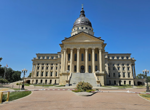 A grand government building with a large dome, columns, and steps, set against a clear blue sky.
