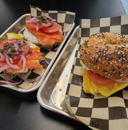 Two bagel sandwiches on a tray: one with smoked salmon, cream cheese, and veggies; the other with an omelet and tomato.