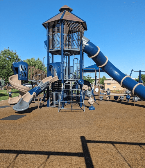 A large playground structure with slides, climbing areas, and a tower, set against a clear blue sky.