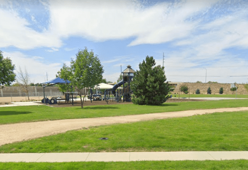 A playground with slides and picnic areas surrounded by grass and trees under a blue sky.