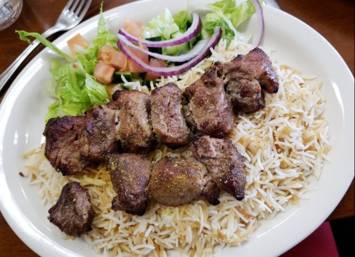 A plate of seasoned grilled meat served over fluffy rice, accompanied by a fresh salad with lettuce, tomatoes, and onions.
