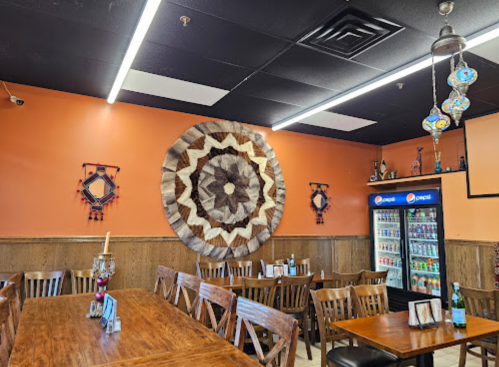 Interior of a restaurant featuring wooden tables, an orange wall with a large decorative piece, and a drink fridge.