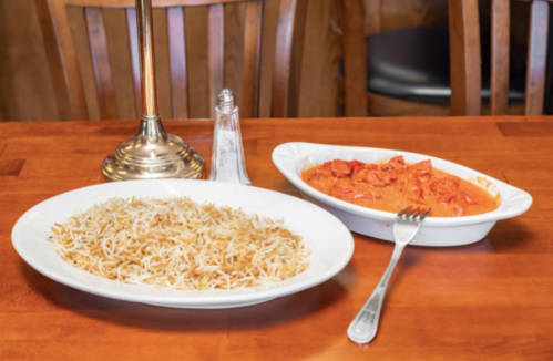 A plate of fluffy rice next to a dish of creamy tomato curry on a wooden table.
