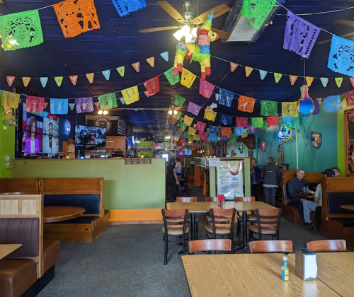 Colorful papel picado decorations hang from the ceiling in a lively restaurant with booths and a bar area.