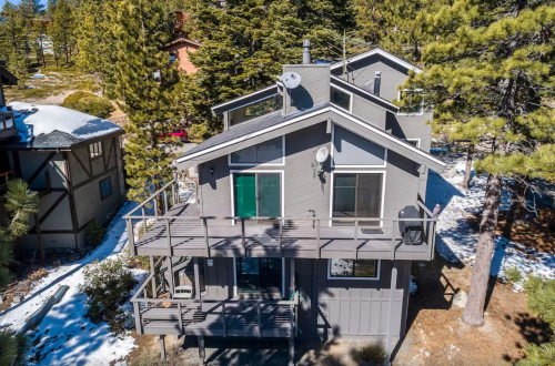 A modern gray house with a deck, surrounded by trees and snow, showcasing a scenic mountain setting.
