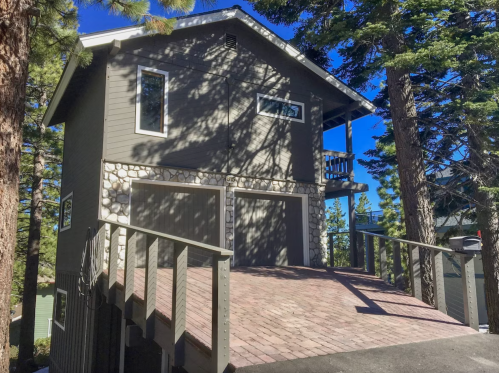 A two-story house with a stone-accented facade, surrounded by tall trees and a paved driveway.