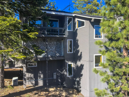 A modern two-story house with stone accents, surrounded by trees and blue sky.