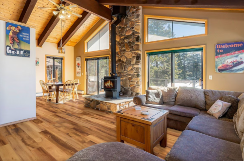 Cozy living room with a stone fireplace, wooden beams, and a dining area, featuring warm lighting and rustic decor.