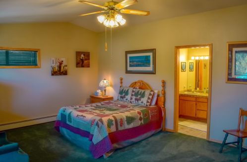 Cozy bedroom with a wooden bed, patterned quilt, and an adjoining bathroom, featuring warm lighting and rustic decor.