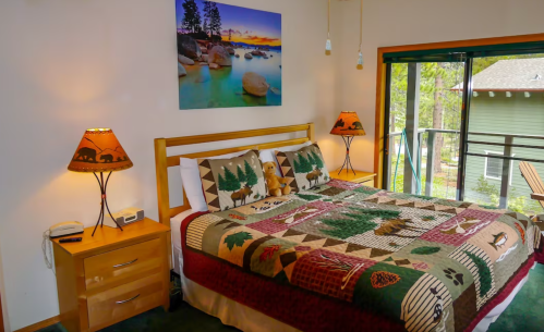 Cozy bedroom with a wooden bed, nature-themed bedding, lamps, and a scenic wall art above a balcony.