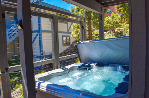 A hot tub on a deck, surrounded by trees and a building in the background, under a clear blue sky.