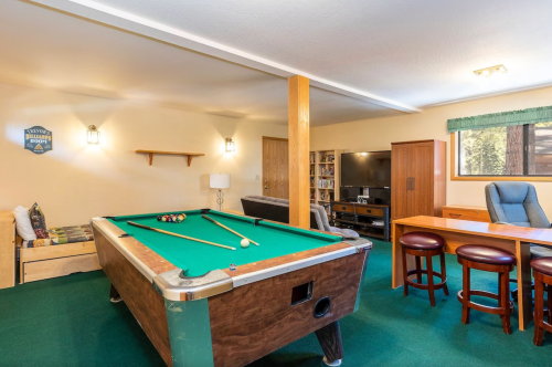 A cozy game room featuring a pool table, seating area, and entertainment center with bookshelves in the background.